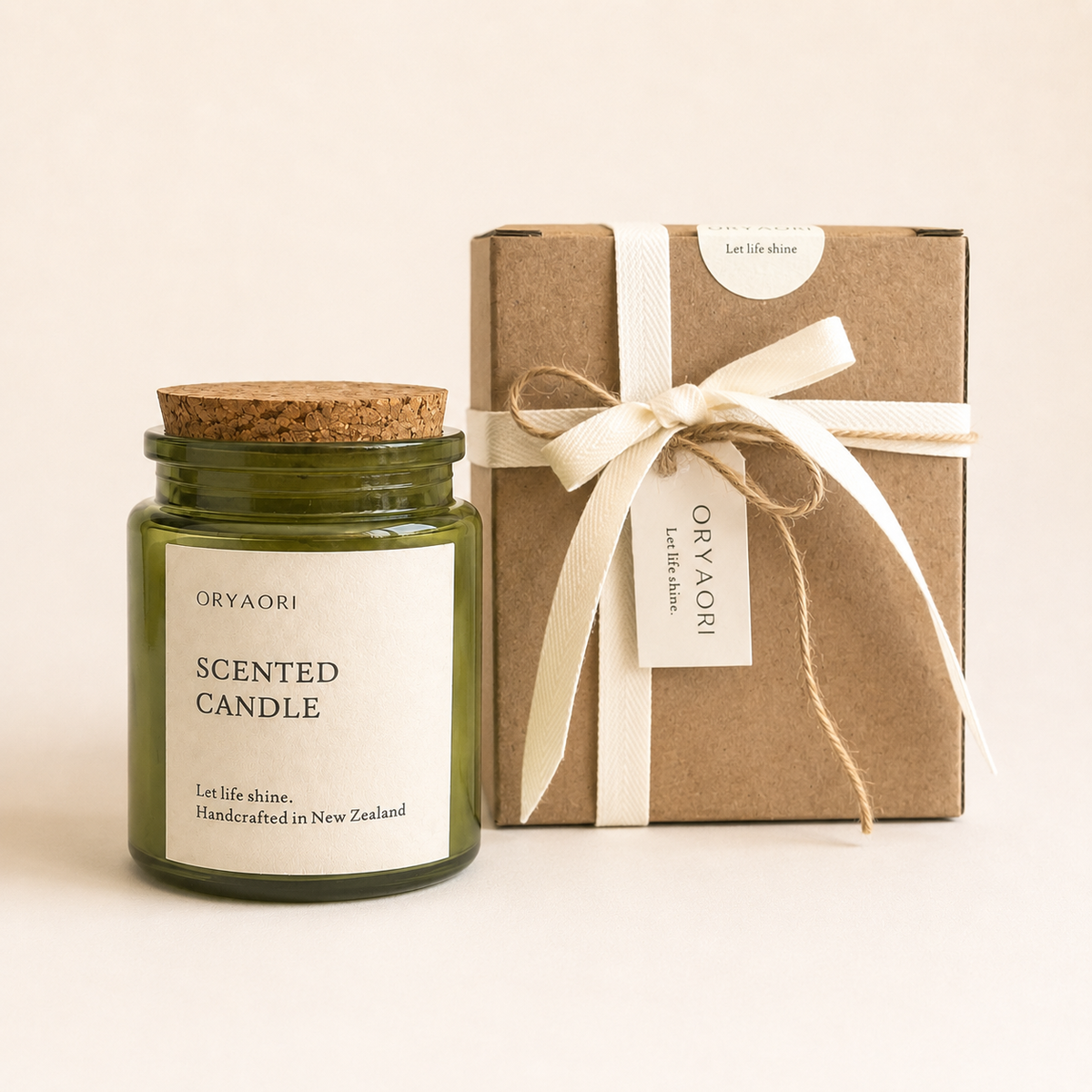 An Oryaori scented candle in a dark green glass jar with a cork lid, shown next to its brown kraft paper gift box tied with a cream ribbon.